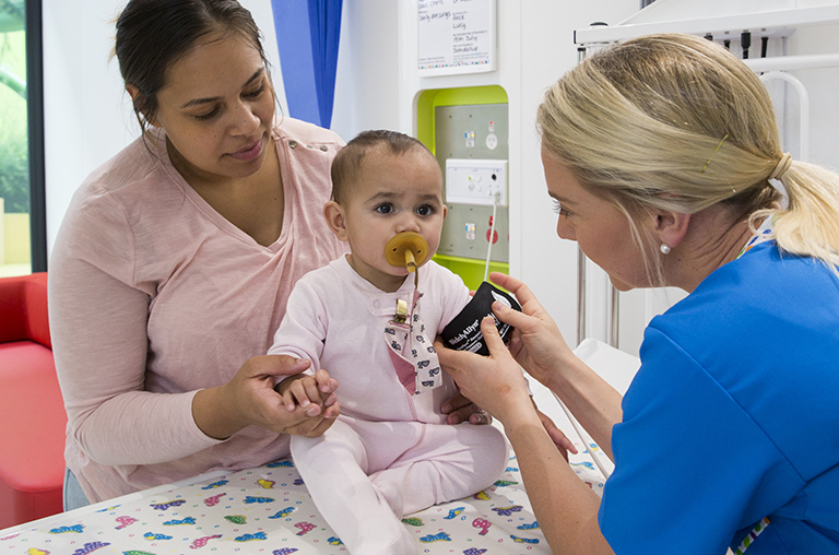 A mother holds her baby girl as a PCH nurse applies a cuff