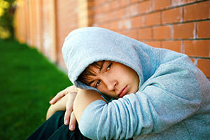 Boy in hoodie sitting against wall