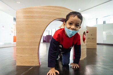 A young boy crawling through an arched opening in the wooden play equipment located at Perth Children's Hospital