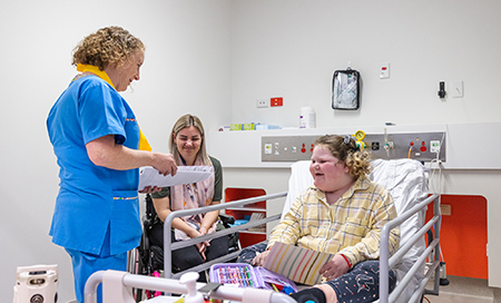 Charlee in a patient bed with a PCH nurse, and her mum