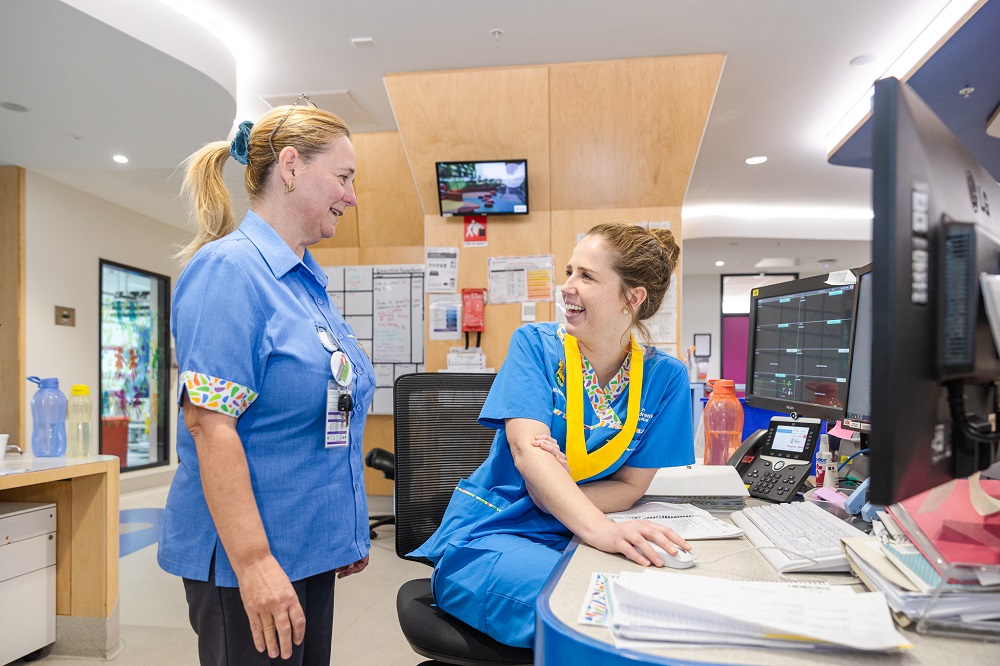 Two PCH nurses working together on the wards, smiling at each other